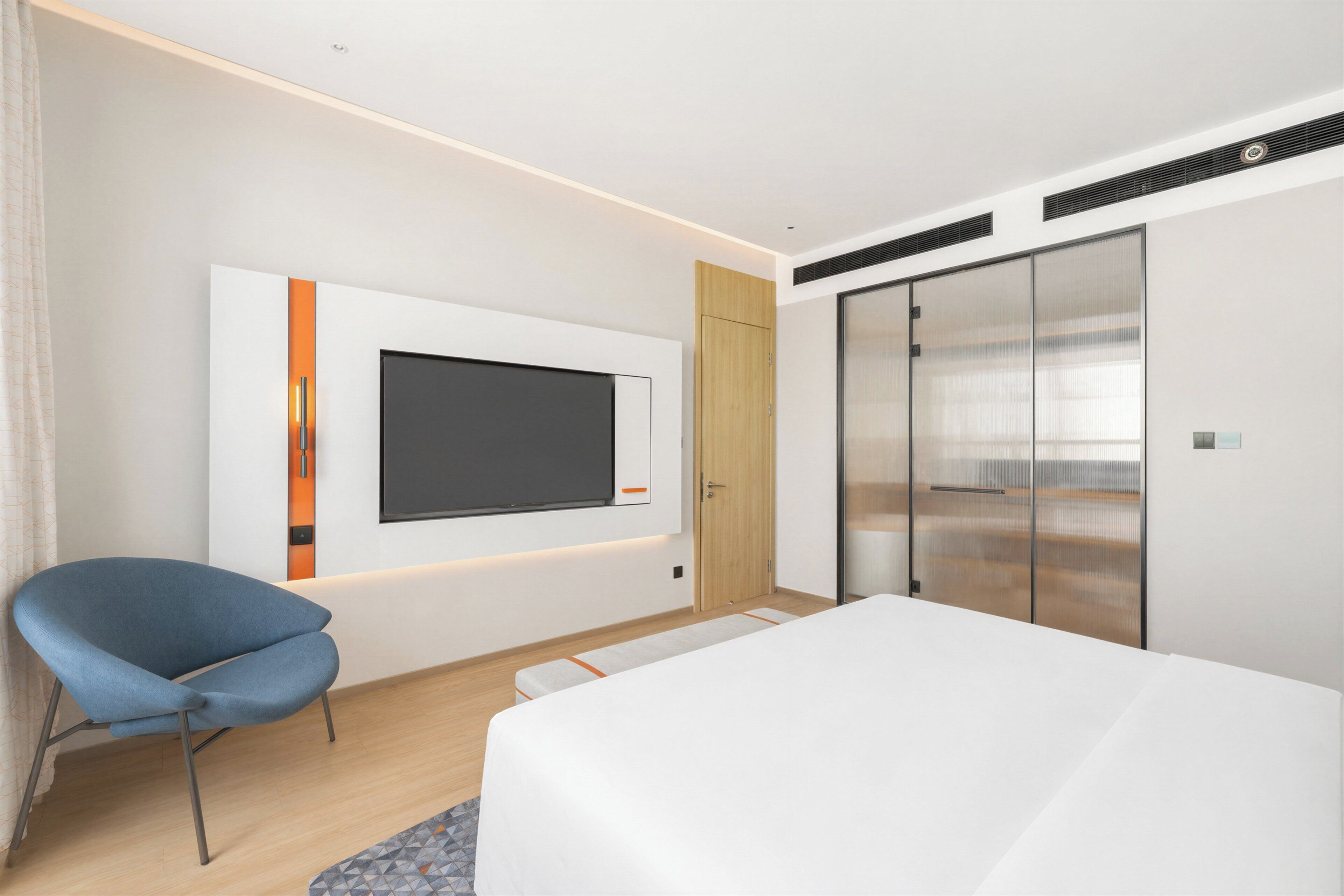 A modern hotel room with a bed, a TV mounted on the wall, a blue chair, and a wardrobe with a sliding door.
