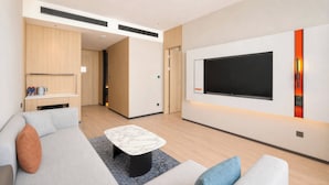 A modern living room with a flat-screen TV mounted on the wall, a sofa, a coffee table, and a small kitchen area with a microwave and coffee maker. - Holiday Inn Express Changbaishan Beauty Pine by IHG (Yanbian)