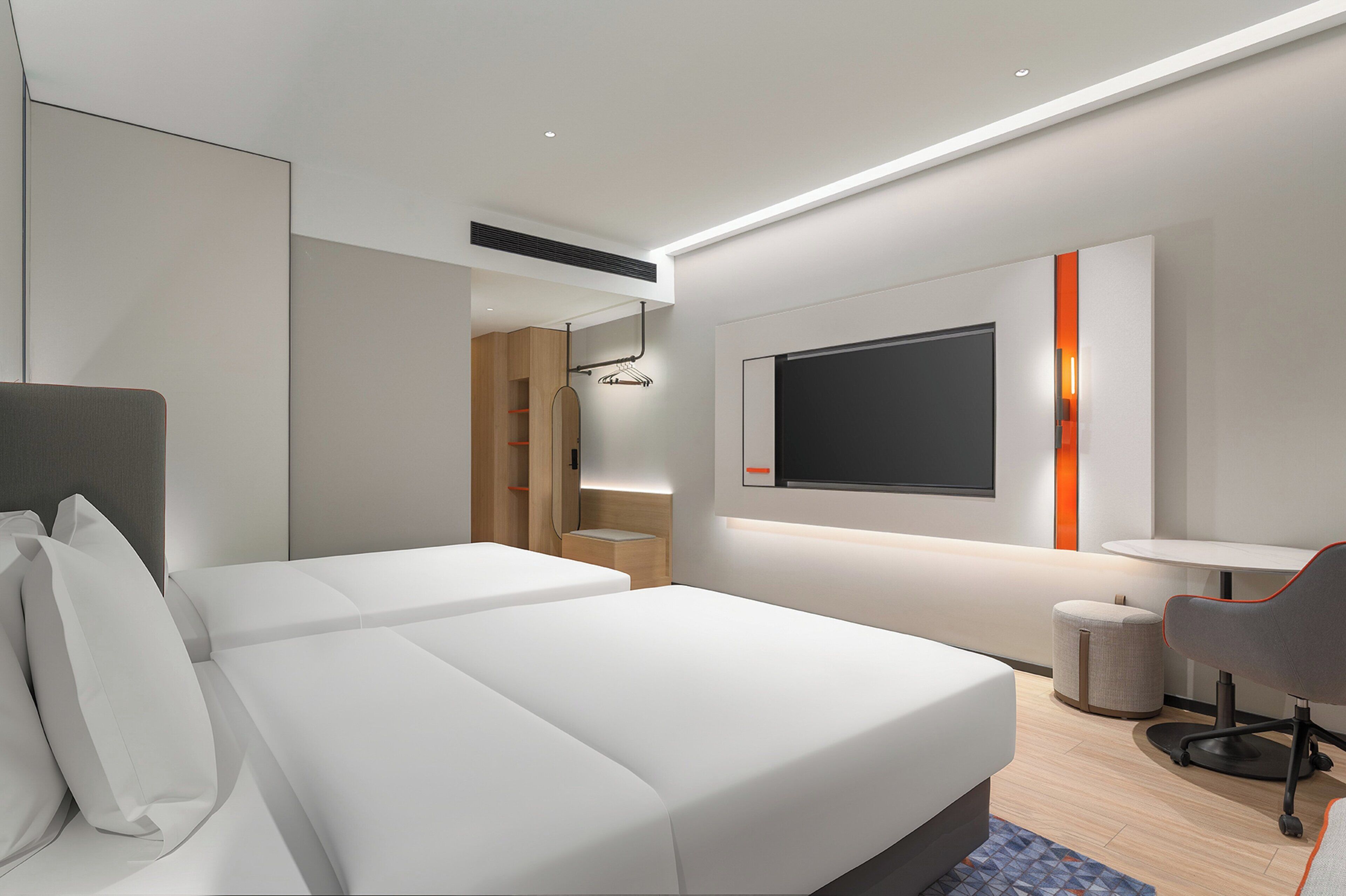 A modern hotel room with a large bed, a desk with a chair, a TV mounted on the wall, and a built-in wardrobe.
