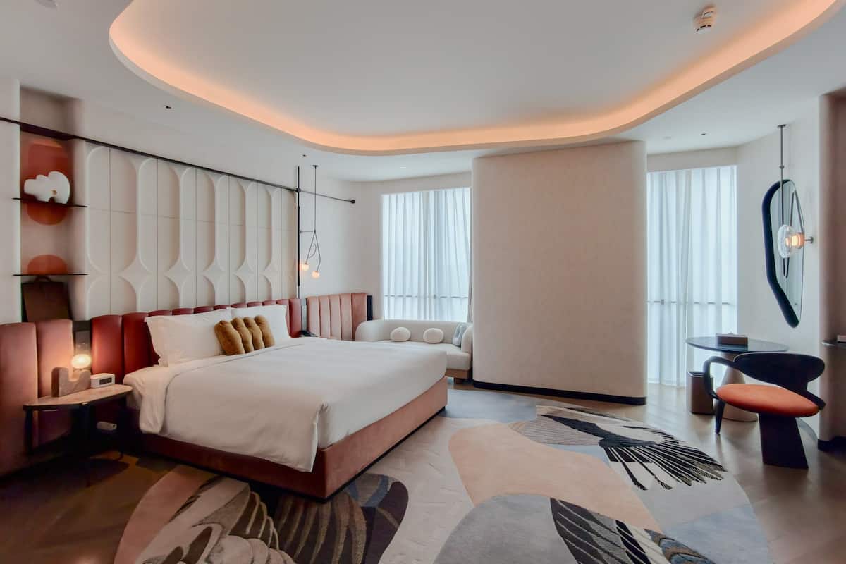 A modern bedroom with a large bed, bedside tables, a seating area, and a large window.