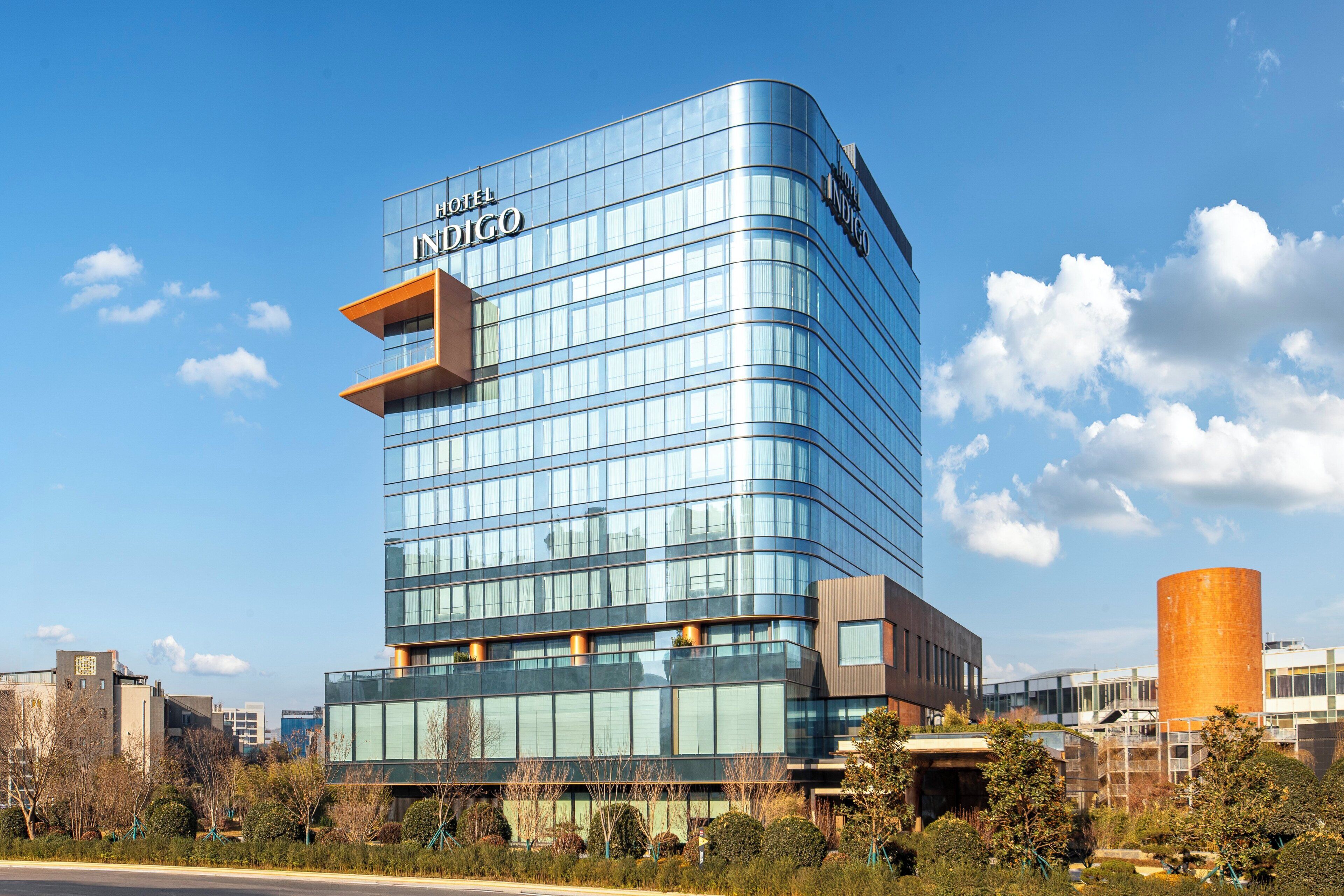 A modern hotel building with a curved facade, large windows, and a prominent "HOTEL INIGO" sign.