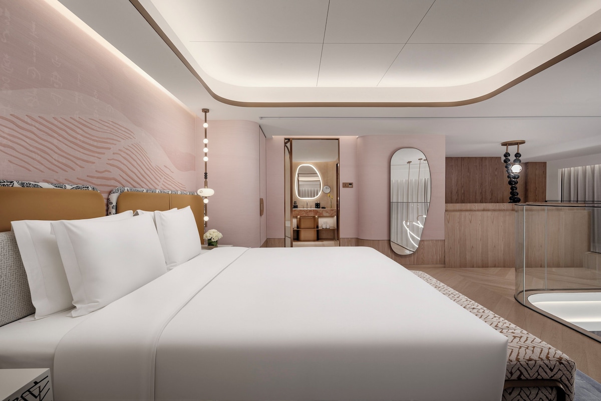 Een moderne hotelkamer met een groot bed, een kaptafel met spiegel en een badkamer met een douchecabine van glas.