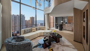 A modern living room with a curved sofa, a coffee table, and a view of a cityscape through large windows. - Hotel Indigo Xi An High Tech Zone by IHG (Xi'an)