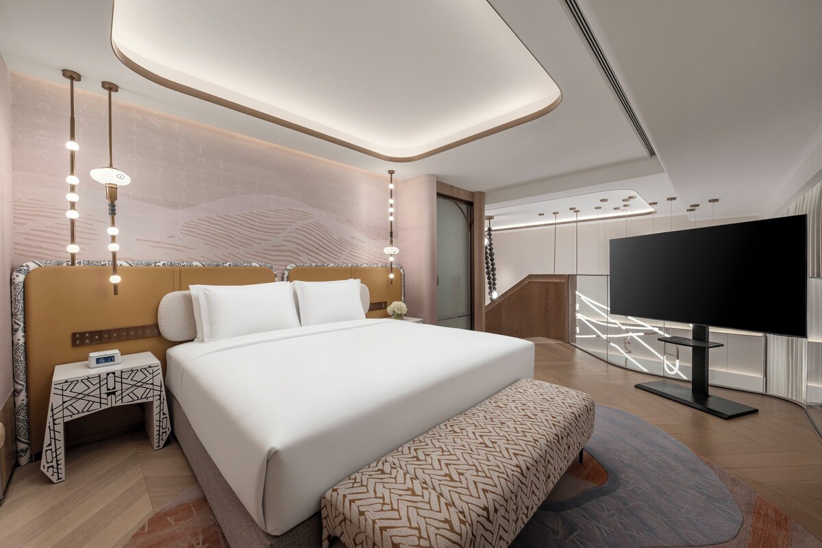 A modern hotel room with a large bed, bedside table, and a flat-screen TV.