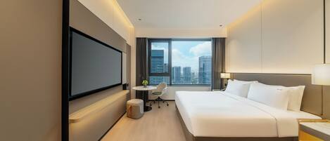 Una habitación de hotel moderna con una cama grande, un televisor de pantalla plana montado en la pared, un escritorio pequeño con una silla y una ventana con vistas a la ciudad.