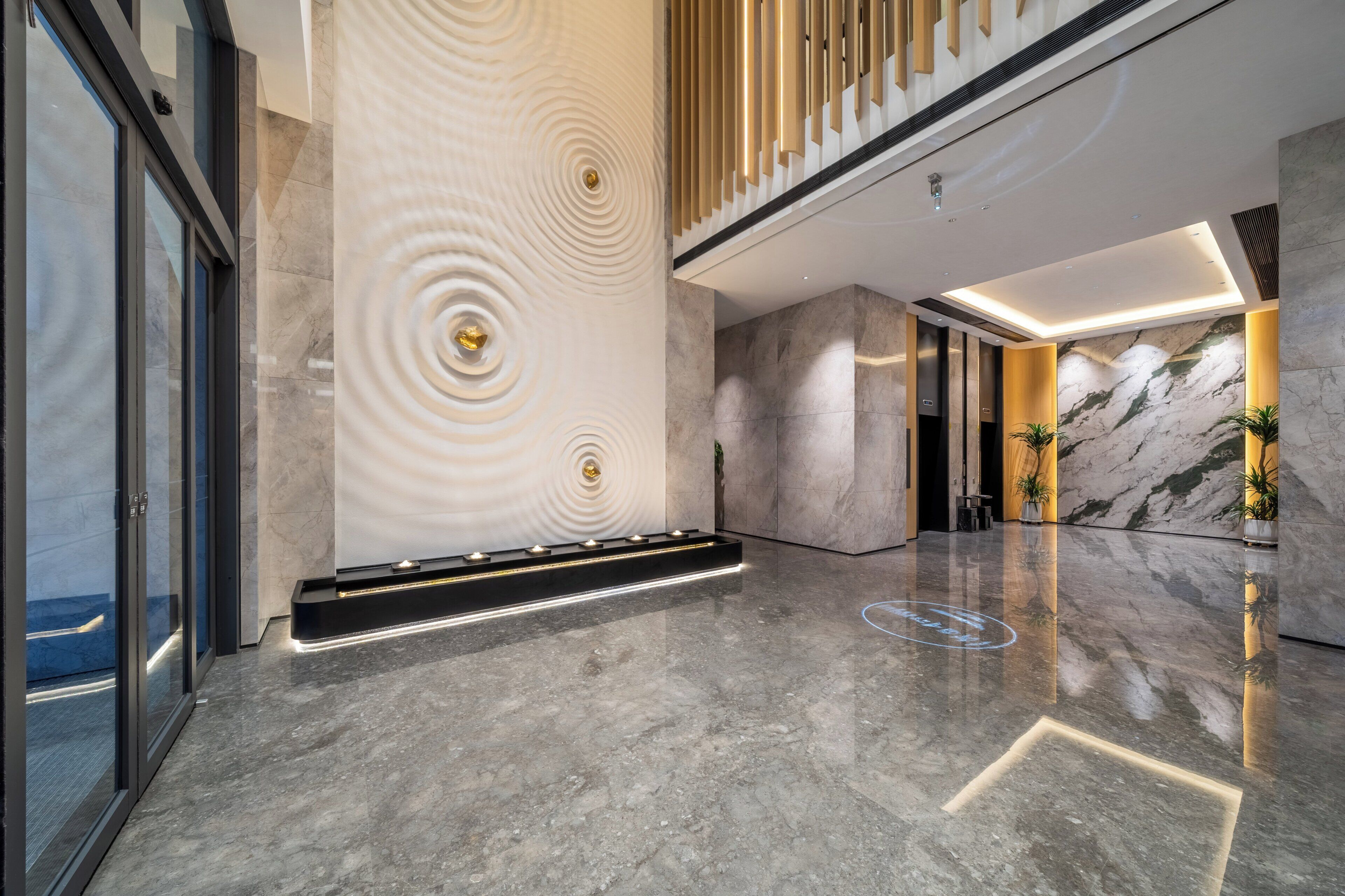 A modern lobby with a marble floor, a central light feature, and a staircase.
