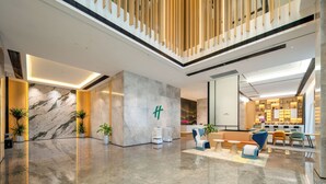 A modern lobby with a marble reception desk, seating area, and a staircase with wooden railings. - Holiday Inn Suzhou North by IHG (Suzhou)