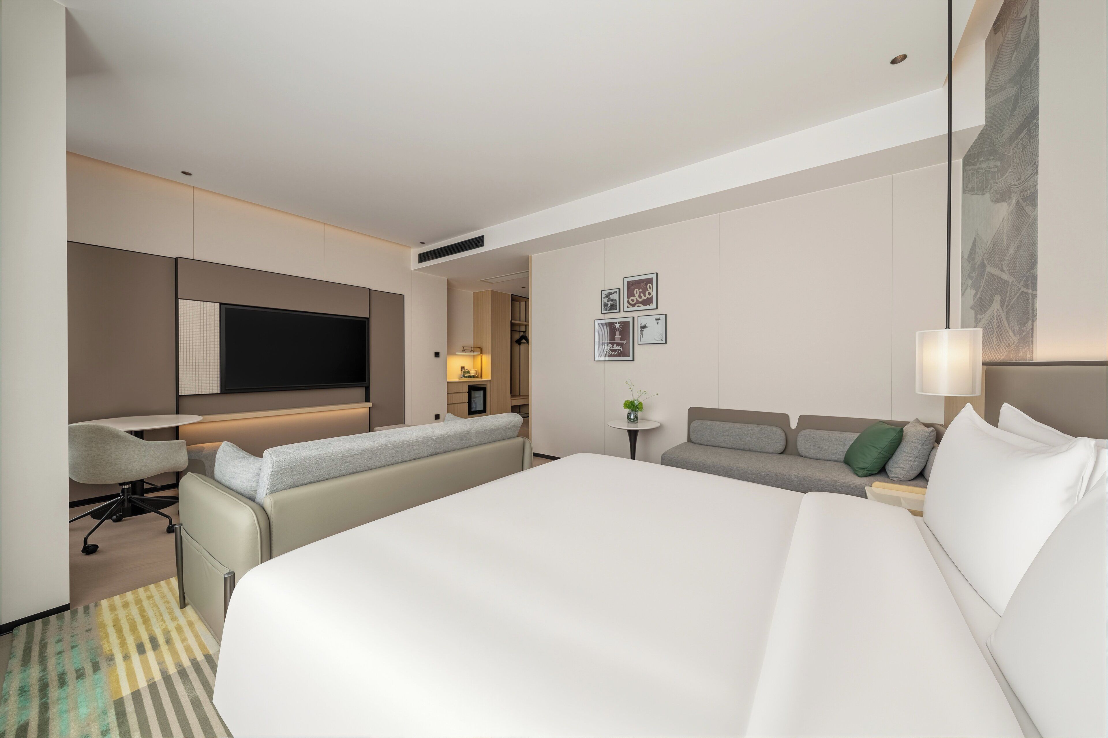 A hotel room with a large bed, a sofa, a desk, and a TV.