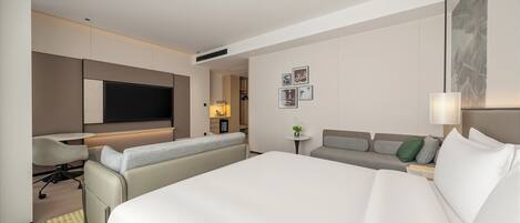 A hotel room with a large bed, a sofa, a desk, and a TV.