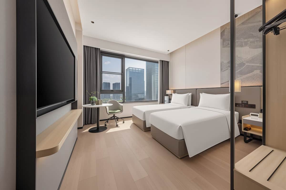 Ein modernes Hotelzimmer mit einem großen Bett, einem Schreibtisch, einem Sessel, einem Fernseher und einem Fenster mit Blick auf die Stadt.