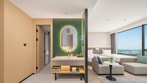 A modern hotel room with a large bed, a sofa, a small table, and a bathroom with a green-tiled wall and a mirror. - Holiday Inn Suzhou North by IHG (Suzhou)