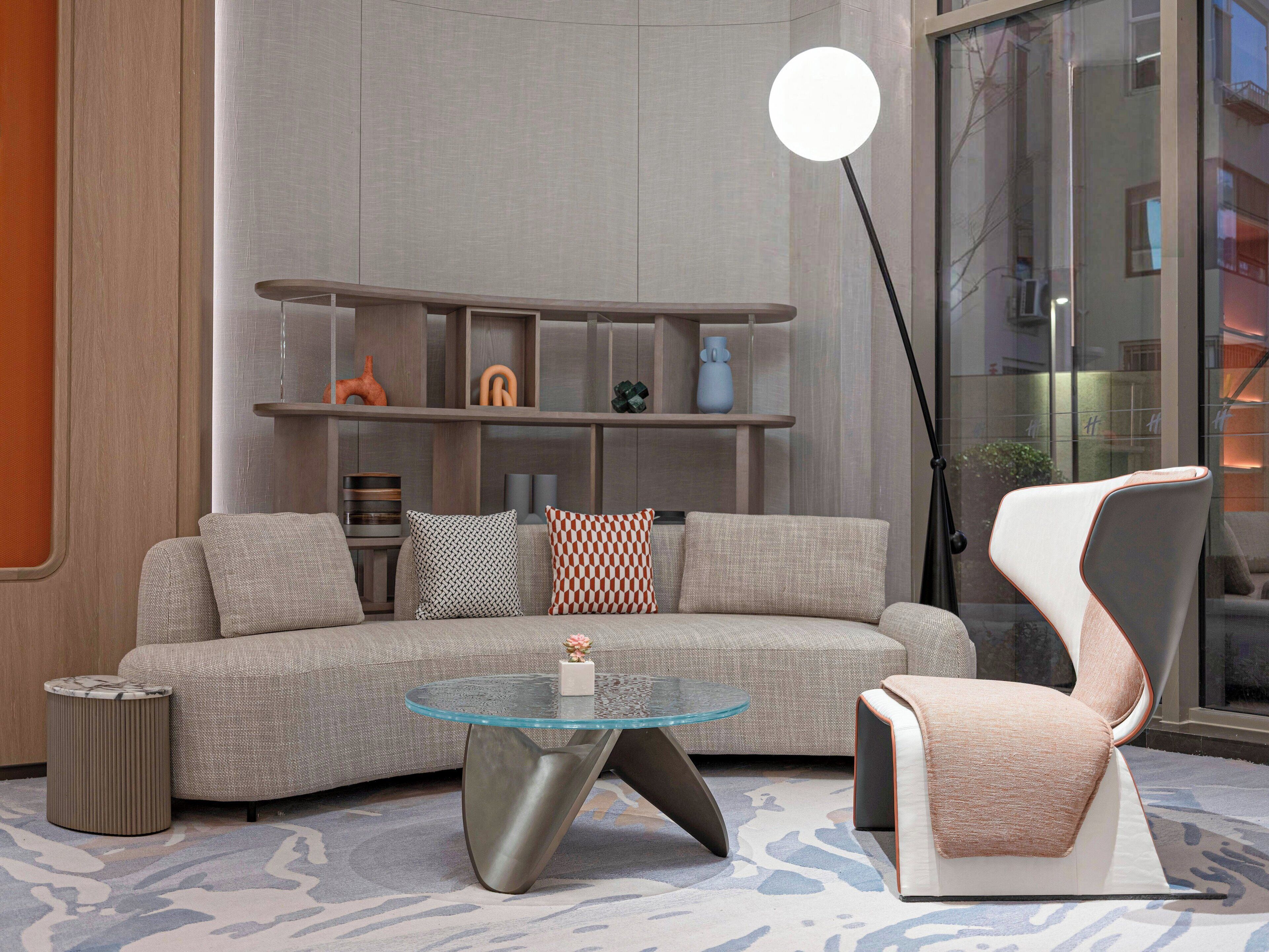 A modern living room with a sectional sofa, a glass coffee table, a unique chair, and a floor lamp.