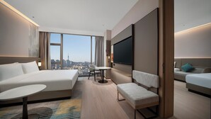 A modern hotel room with a large bed, a desk, a chair, a TV, and a view of the cityscape. - Holiday Inn Qingdao CBD by IHG (Qingdao)