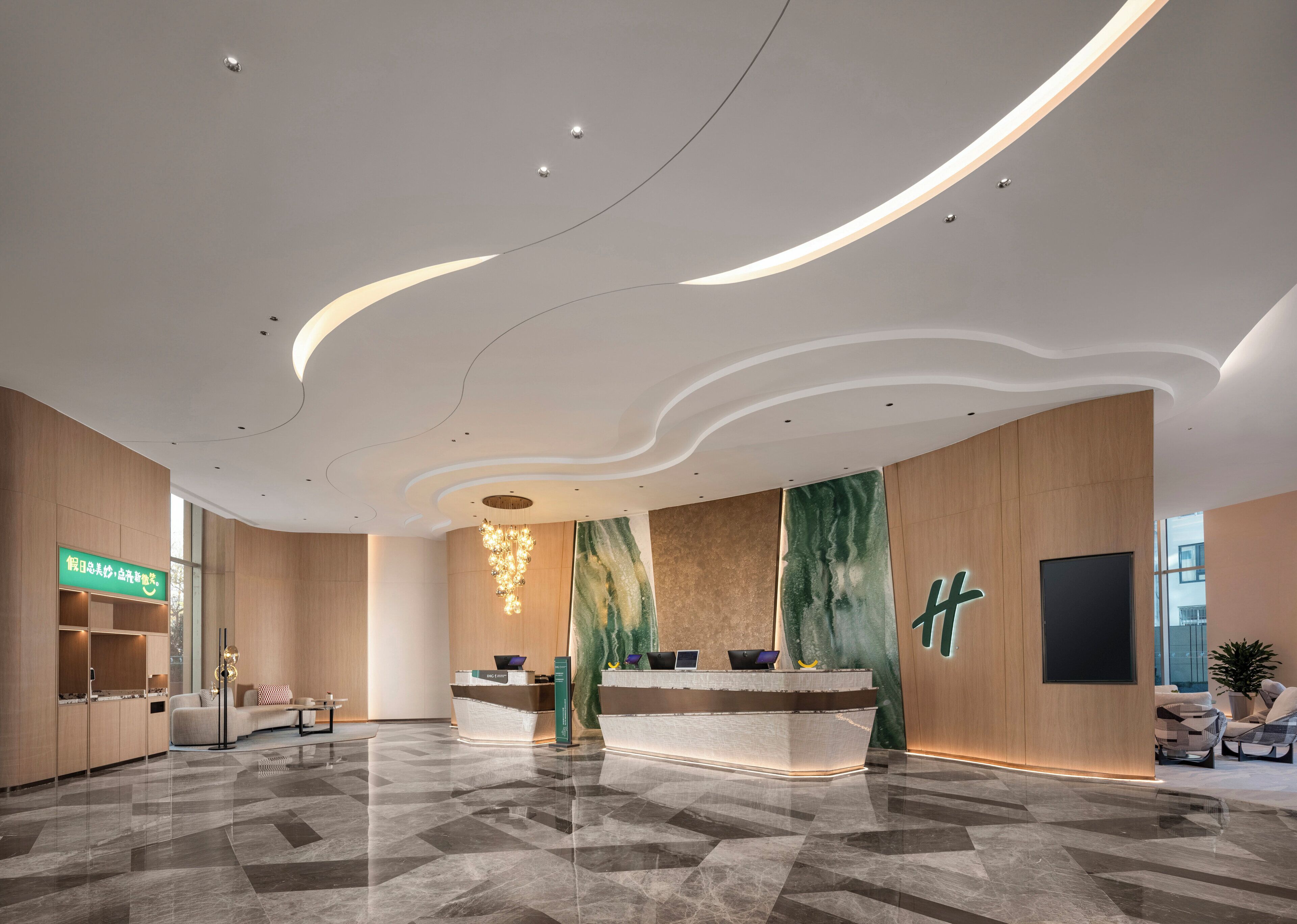 Een moderne hotellobby met een receptiebalie, zithoek en een grote groene marmeren wand.