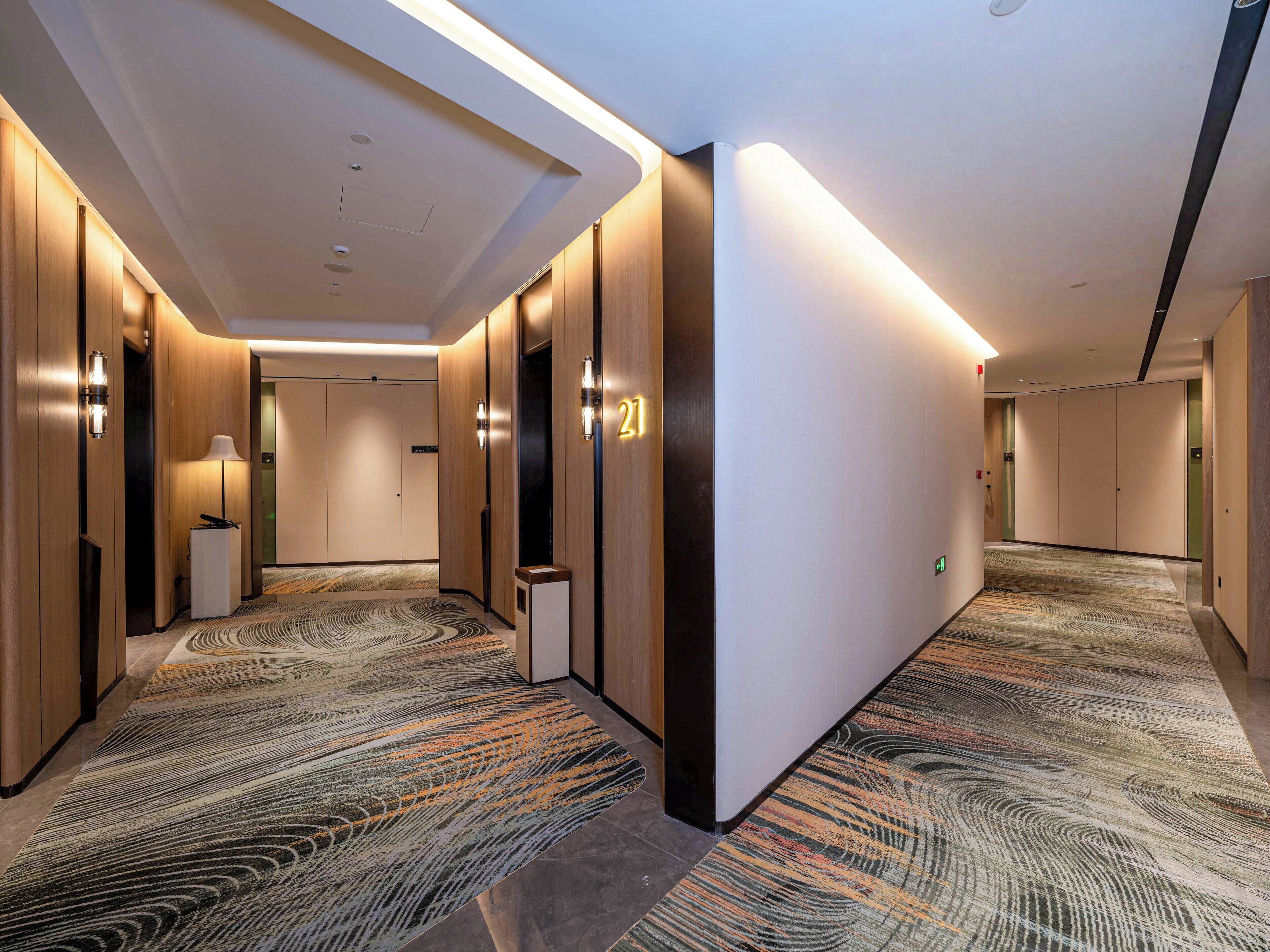 Ein Hotelgang mit Holzwandverkleidung, einem gemusterten Teppich und einem modernen Deckenstil.