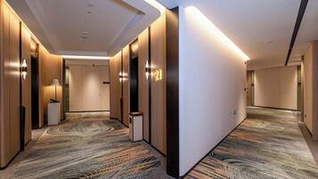 Ein Hotelgang mit Holzwandverkleidung, einem gemusterten Teppich und einem modernen Deckenstil.