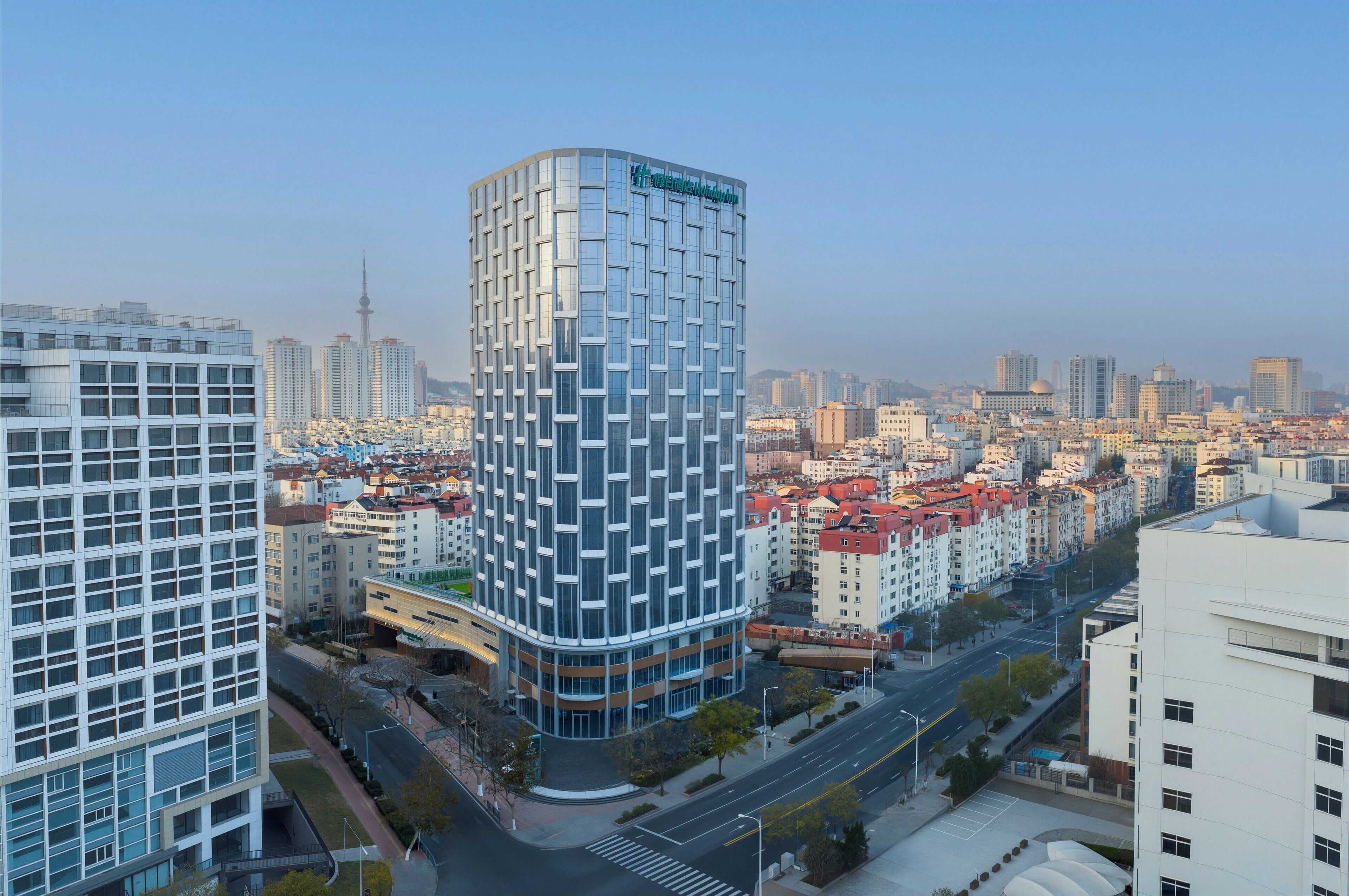 Un hôtel moderne à la façade géométrique originale, entouré d’un paysage urbain composé de différents bâtiments et surplombant un ciel dégagé.