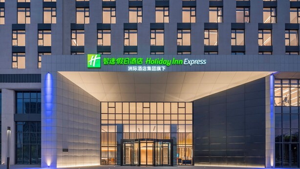 A modern hotel entrance with a glass facade and illuminated signage. - Holiday Inn Express Gongyi City Center by IHG (Zhengzhou)