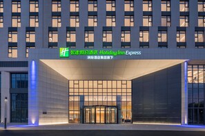 A modern hotel entrance with a glass facade and illuminated signage. - Holiday Inn Express Gongyi City Center by IHG (Zhengzhou)