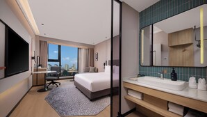 A modern hotel room with a large bed, a desk, a city view, a bathroom with a sink and mirror, and a large window. - Holiday Inn Express Gongyi City Center by IHG (Zhengzhou)