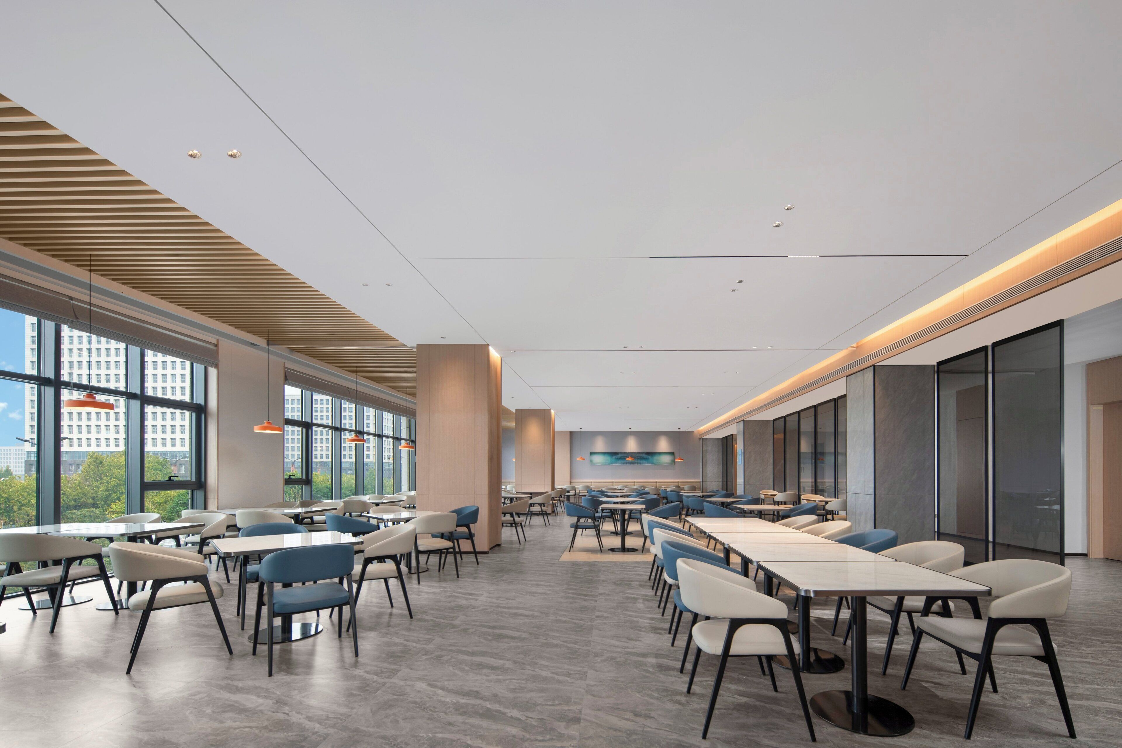 A spacious indoor dining area with high ceilings, large windows, and modern furniture.
