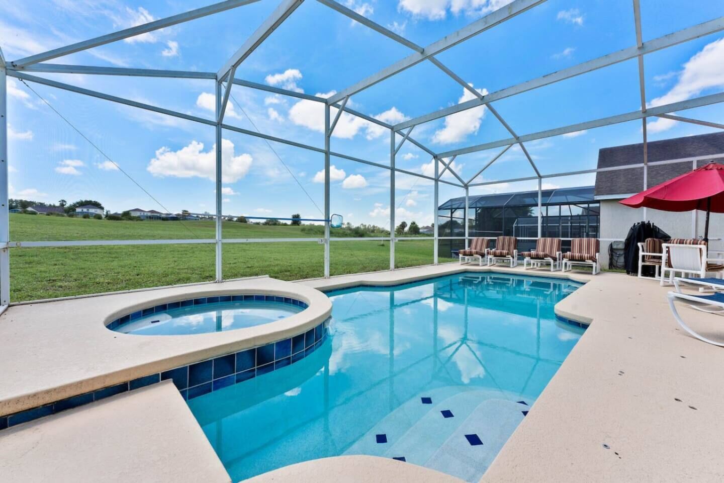 A swimming pool with a hot tub, lounge chairs, and a covered area with a red umbrella.
