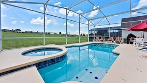 A swimming pool with a hot tub, lounge chairs, and a covered area with a red umbrella.