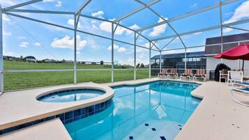 A swimming pool with a hot tub, lounge chairs, and a covered area with a red umbrella.