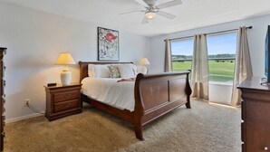 A bedroom with a bed, nightstands, a ceiling fan, a window with curtains, and a painting on the wall.