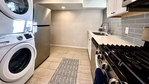 A compact kitchen with a washing machine, a microwave, and a stove. - The Cozy Below (Edgewater)