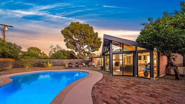 Une maison moderne dotée d’une piscine, d’un patio fermé par des baies vitrées et d’un espace patio en briques.