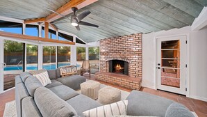 Un salon moderne avec un grand canapé d’angle gris, une cheminée en briques et un ventilateur de plafond.