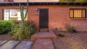 Une maison en briques avec une porte noire, une plaque de numéro et un cactus dans le jardin.