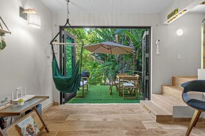 Un intérieur moderne agrémenté d’un fauteuil suspendu, d’une table avec des chaises et d’un escalier menant à un espace extérieur verdoyant.