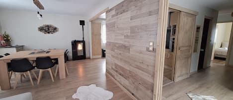 A modern living room with a wooden floor, a dining area with a table and chairs, a fireplace, and a large wooden partition.