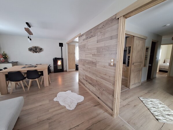 A modern living room with a wooden floor, a dining area with a table and chairs, a fireplace, and a large wooden partition.