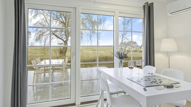 A modern room with a white table and chairs, a view of a deck with outdoor furniture, and a lamp on the right.