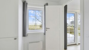 A room with a white door, a window with a view of a grassy field, and a radiator.