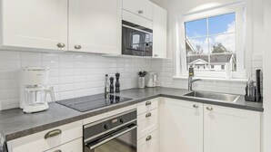 A modern kitchen with white cabinets, a black microwave, a coffee maker, and a window with a view of houses.