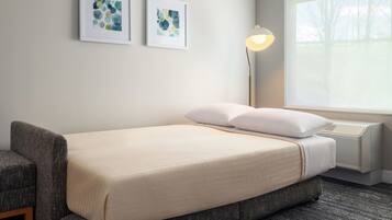 A hotel room with a bed, a chair, a standing lamp, and two framed artworks on the wall.