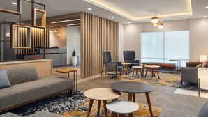A modern hotel lobby with a sofa, chairs, tables, and a large window. - Towneplace Suites By Marriott Hickory (Hickory)