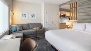 A hotel room with a bed, a sofa, a small table, a chair, a desk, a microwave, a lamp, and artwork on the walls. - Towneplace Suites By Marriott Hickory (Hickory)