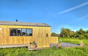 Un bâtiment moderne en bois, doté de grandes fenêtres, d’un toit plat et d’une terrasse dallée.