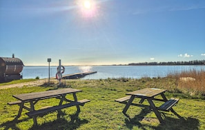 Ein Picknickplatz am Seeufer mit zwei Holztischen und einem Grill.