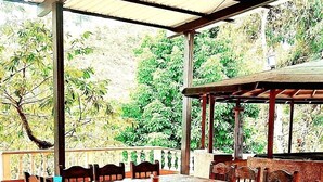 A covered outdoor dining area with a round table and chairs, surrounded by a tiled floor and a metal roof. - Hotel pekin (San Carlos)