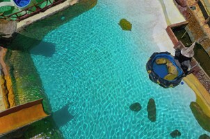 Una piscina azul cristalina con un bote pequeño y un tobogán.