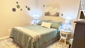 Ein Schlafzimmer mit einem Bett, Nachttischen, einer Lampe, einem Bild und Wandblumen zur Dekoration.
