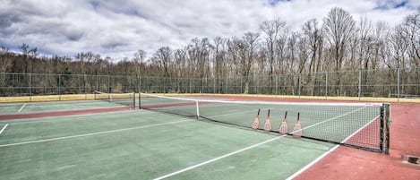 A tennis court with a net, surrounded by a fence, and trees in the background.