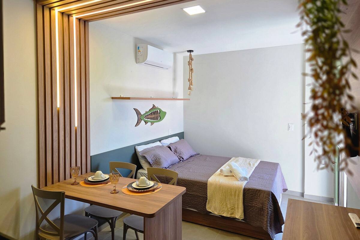A room with a bed, a table with chairs, a wall-mounted air conditioner, and a fish decoration.