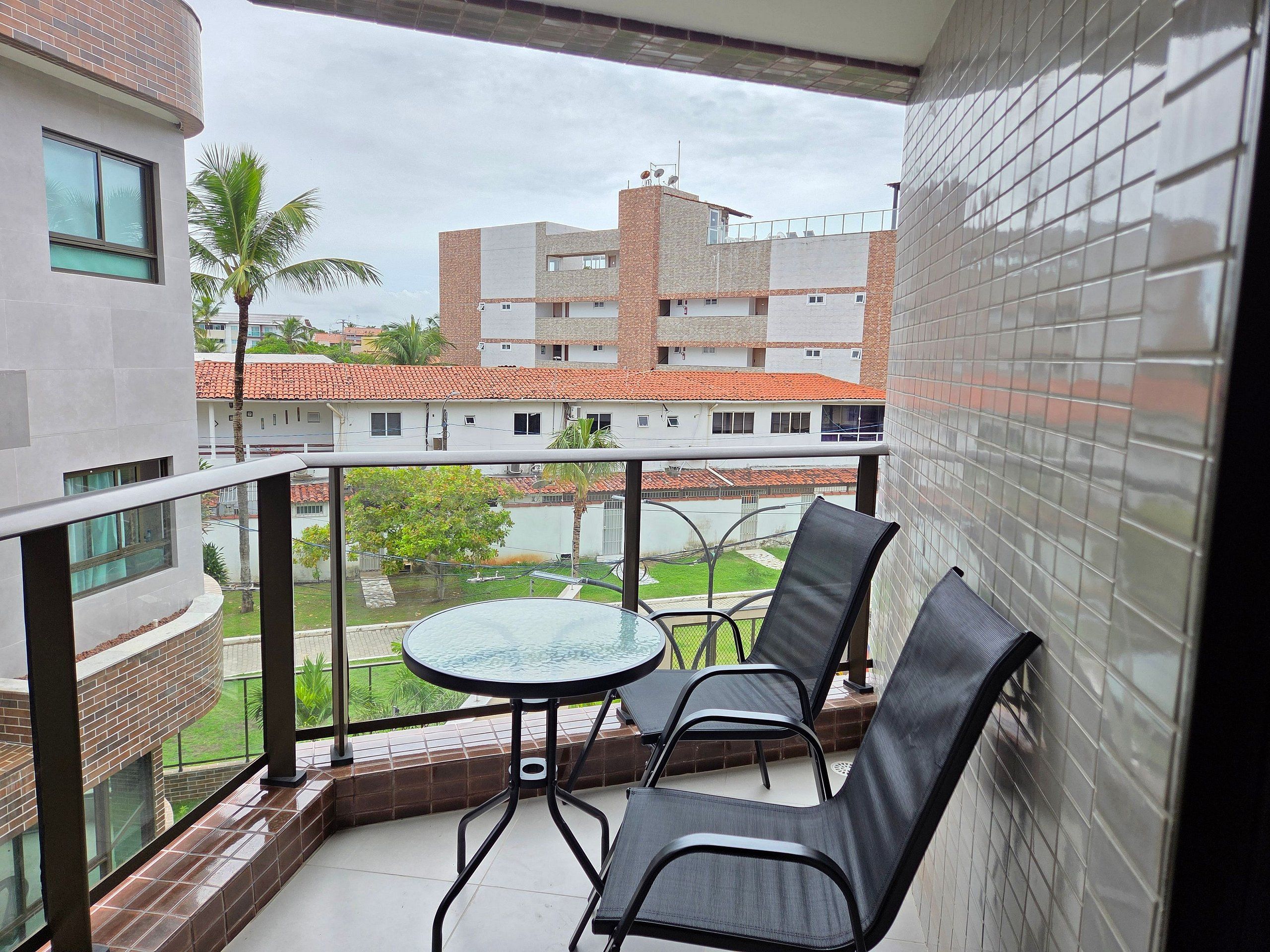 Un balcón con una mesa de vidrio y dos sillas, con vistas a una zona residencial con edificios y áreas verdes.